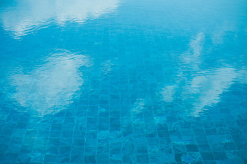 Close up blue water in swimming pool reflection white clouds and blue sky. (Soft focus)