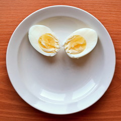 two halves hard boiled chicken egg on a white saucer and wooden table 