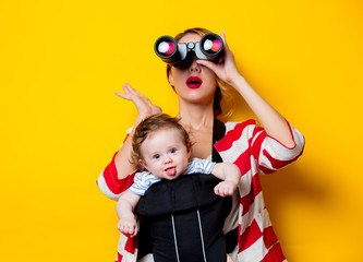 little baby in carrier and mother with binoculars on yellow background