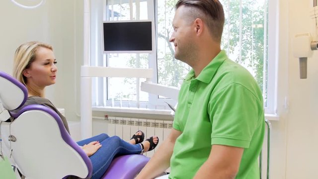 4k footage of beautiful blonde woman sitting in dentist chair and showing aching tooth to dentist