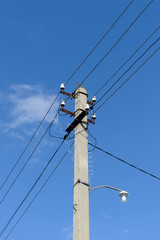 concrete column with power lines and a lamp against a blue sky
