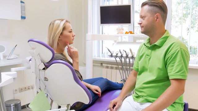 4k footage of handsome male dentist talking to his woman patient sitting in dental chair
