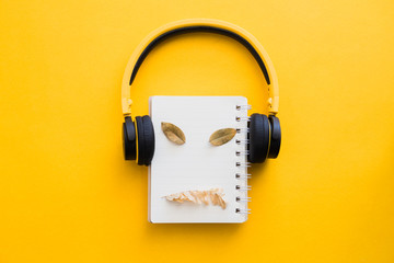 Yellow headphone with blank notebook and dry leaves on yellow paper background