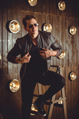 Fototapeta na wymiar Handsome young man. Fashionable man in leather jacket is sitting on loft background. dramatic fashion male model 