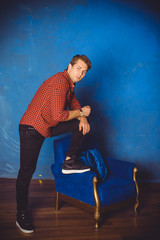 Handsome young man. Fashionable man in plaid shirt is sitting on blue interior background. Nice fashion male model  