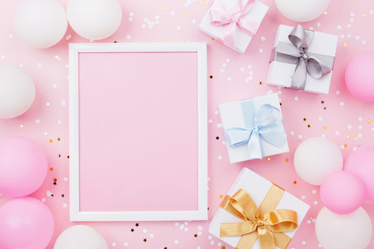 Birthday or holiday mockup with frame, gift box, pastel balloons and confetti on pink table top view. Flat lay composition.