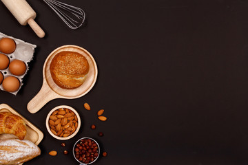 Homemade breads or bun, croissant and bakery ingredients, flour, almond nuts, hazelnuts, eggs on dark background, Bakery background frame, Cooking breakfast concept. Flat lay, Top view and copy space.