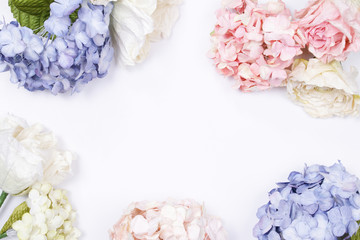 Frame made of pink and beige roses, green leaves, blue hydrangea, branches on white background. Flat lay, top view. Wedding's background. Valentine's background with copy space.