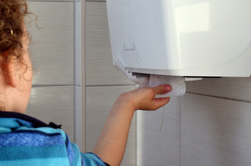Kind zieht Papierhandtuch aus einem Spender einer Toilette