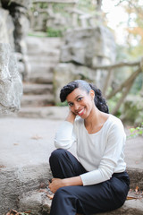 Beautiful half american nigerian female person sitting in park near stone stairs and wearing white...