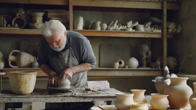 Experienced ceramist is creating utensils from clay on throwign wheel in workshop. Producing eathenware, handmade utensils and professional pottery concept.