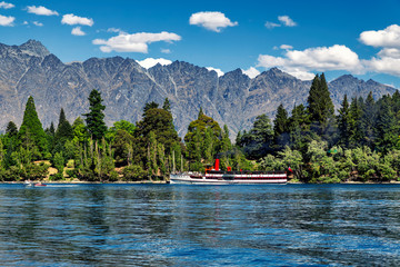 Steam-powered ship on lake Wakatipu surrounded by coniferous forest and mountains in Queenstown,...