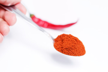 Man's hand holding teaspoon with pepper powder. Red hot chilli pepper in background