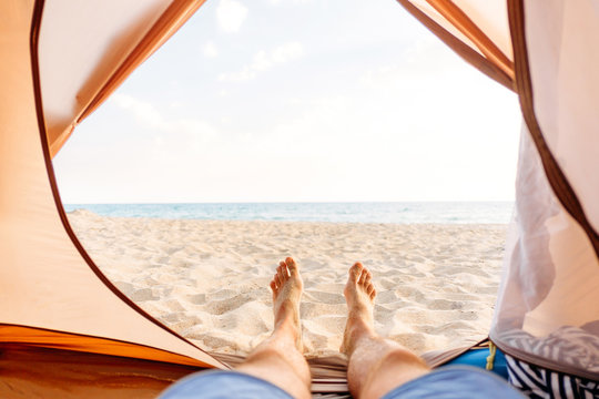 Man resting in a tent on sand beach.