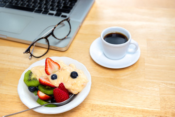 Breakfast bowl of fresh fruits salad with yogurt and coffee and laptop