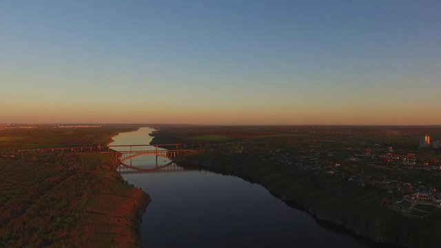 Flight over the wooded coastline of a large river next to a large city during sunset. Dnieper River, Zaporozhye, Ukraine.