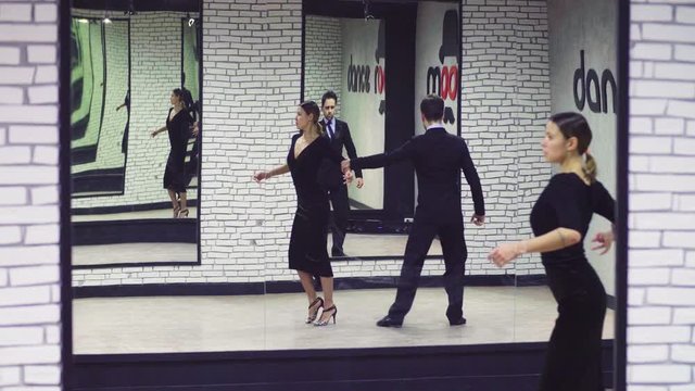 Professional dancing couple in black suits dancing tango in the ballroom. Two mirrors opposite each other create a lot of reflections