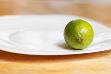 Green lime on the white plate and wooden table