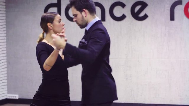 Portrait of professional dancing couple in black suits dancing tango in the ballroom.