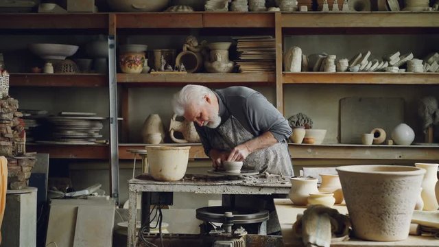 Experienced ceramist is creating utensils from clay on potter's wheel in workshop. Producing eathenware, handmade utensils and professional pottery concept.