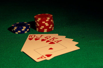 Royal flush of Hearts and poker chips on a green table