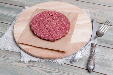 Raw beef hamburger with spices on a round wooden cutting board