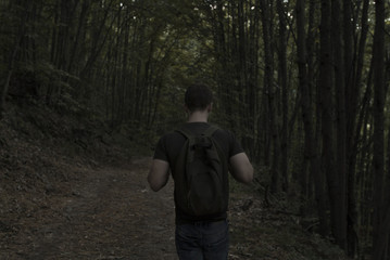 Young man with a backpack exploring a dark forest
