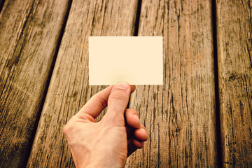 man's hand showing a business card, wooden texture on background (warm tone vintage effect)
