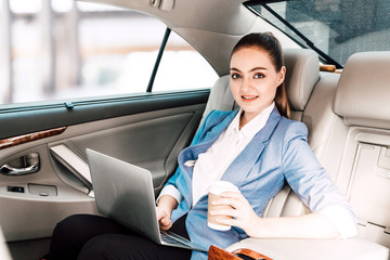 Fototapeta na wymiar Businesswoman work with laptop computer and holding cup of coffee in back seat of luxury car