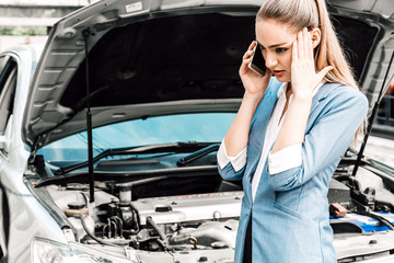 Woman calling for assistance with broken down car engine on street