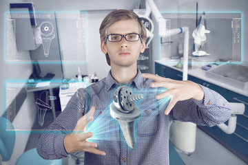 Futuristic medical scientist workplace. Male / man wearing shirt and glasses holding holographic prosthesis of knee and looking at virtual screens making medical analysis on futuristic backgrounв
