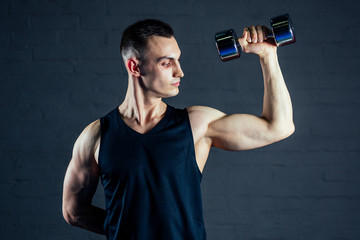 Fototapeta na wymiar young man strengthens the muscles of the hands of dumbbells in the gym on a black background