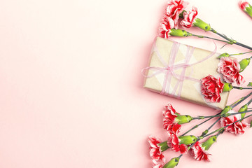 Mother's Day background with carnations flowers and gift box on pink. Copy space.