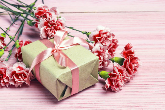 Gift box with carnations flowers on pink wooden background.