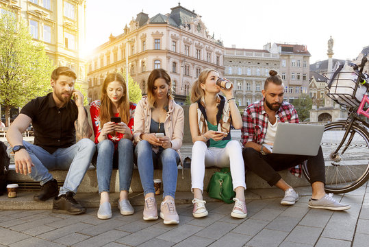 Gl&uuml;ckliche Studenten genie&szlig;en ihren sorglosen Lebensstil in der Stadt sitzen auf der Stra&szlig;e mit Gadgets an einem sonnigen Nachmittag