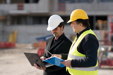 Civil engineer giving instructions to a construction worker using a computer laptop. Outdoors