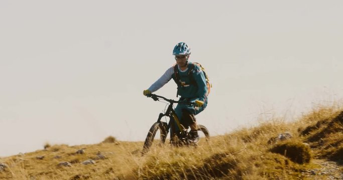 Front View Of Mountain Biker Riding Down Hill Against A Blue Sky.