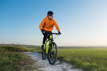 A cyclist in an orange hoodie rides a bike along a mountain path. The concept of extreme sports. Training in the mountains.