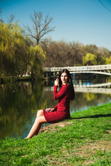  beautiful young brunette with long hair in a park on a spring in spring among flowering trees in a red dress in hands holds magnolia flowers