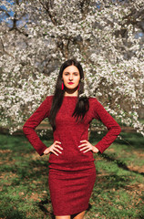 beautiful young brunette with long hair in a park on a spring in the middle of flowering trees in a red dress