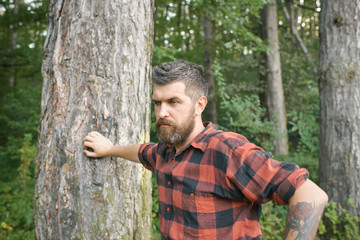 Handsome guy hiking in forest. Brutal lumberjack leaning on tree. Surviving in wilderness