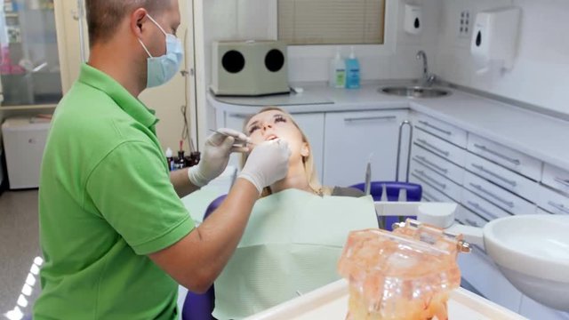 4k footage of camera focusing on table with plastic teel model and protective UV glasses while dentist treatens patient's teeth