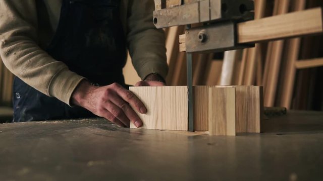 Close up view of a carpenter cutting a wood into pieces. Works with electric saw machine. Wood dust on the surface