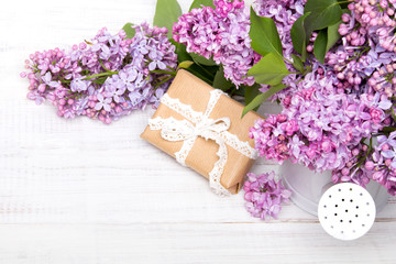 Lilac flowers and gift box on white wooden background, copy space