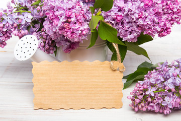 Lilac flowers and empyt card on white wooden background, copy space