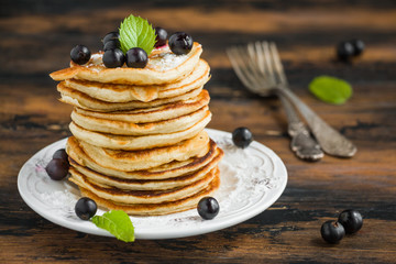 Stack of sweet pancakes with fresh berries and mint on white plate on wooden rustic table
