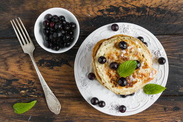Sweet pancakes with black currant and powdered sugar on white plate on wooden rustic table, top view