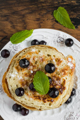Sweet pancakes with black currant and powdered sugar on white plate on wooden rustic table, top view, close-up.