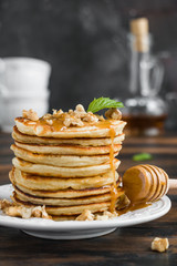 Stack of pancakes with honey and walnuts on white plate on wooden rustic table