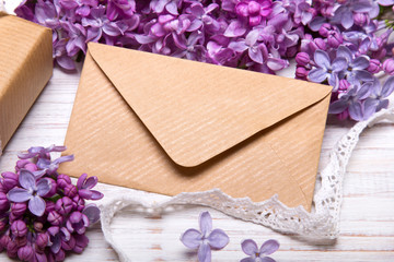 Fototapeta na wymiar Lilac flowers and envelope on white wooden background, copy space